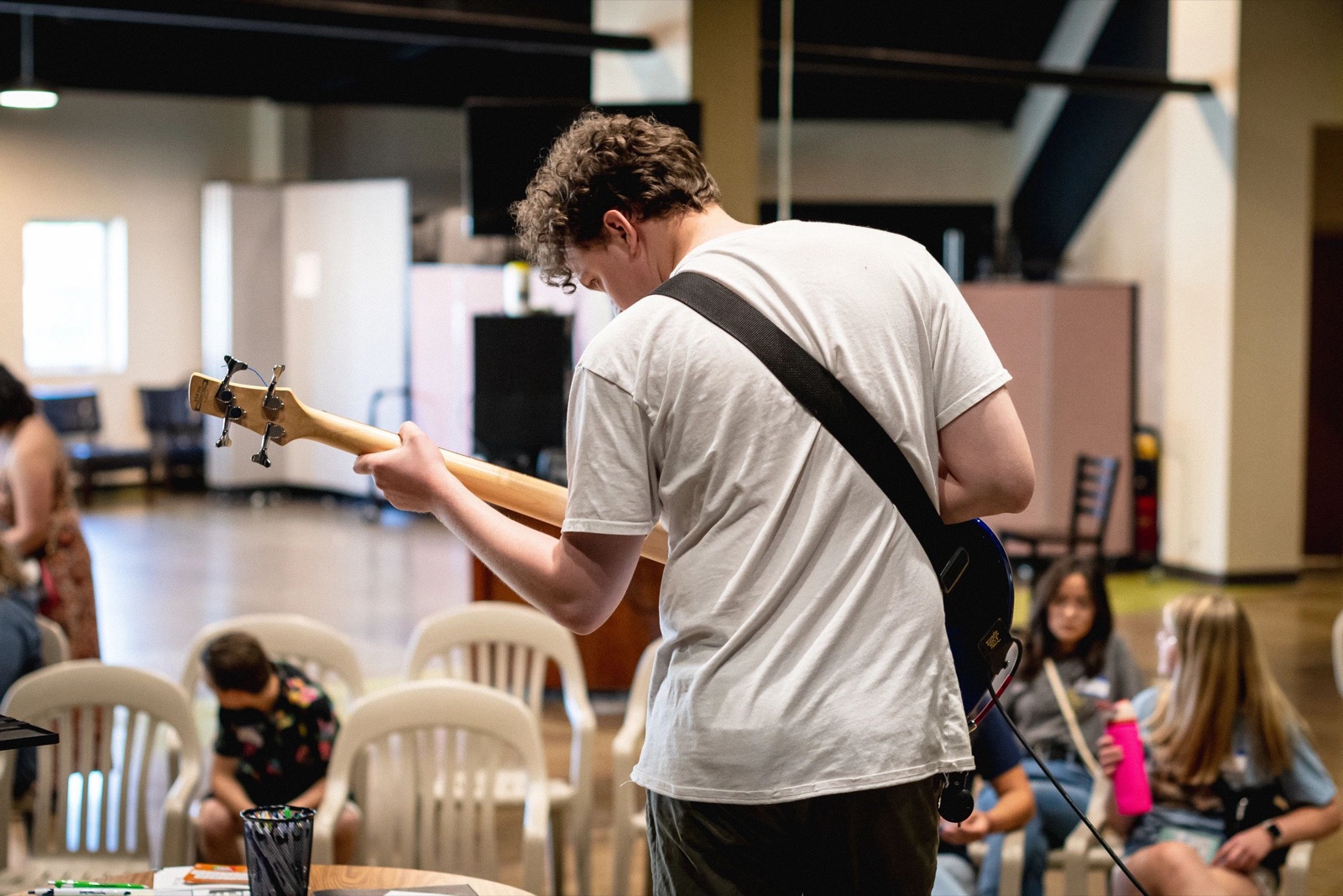 Young man playing bass guitar in a casual indoor setting.